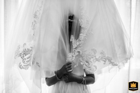 In a black and white detail shot at the bride's house during preparations, the bride's daughter, not in the best mood, hides playfully in her mother's wedding dress, capturing a tender and relatable moment.